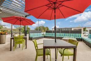 Un espace extérieur aménagé en terrasse, avec des sièges et des tables, des parasols rouges et une vue sur le ciel.