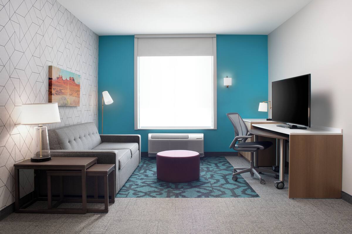 Ein modernes Hotelzimmer mit einer Couch, einem Schreibtisch, einem Fernseher und einem Bild an der Wand.
