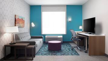 A modern hotel room with a sofa, desk, TV, and a painting on the wall.