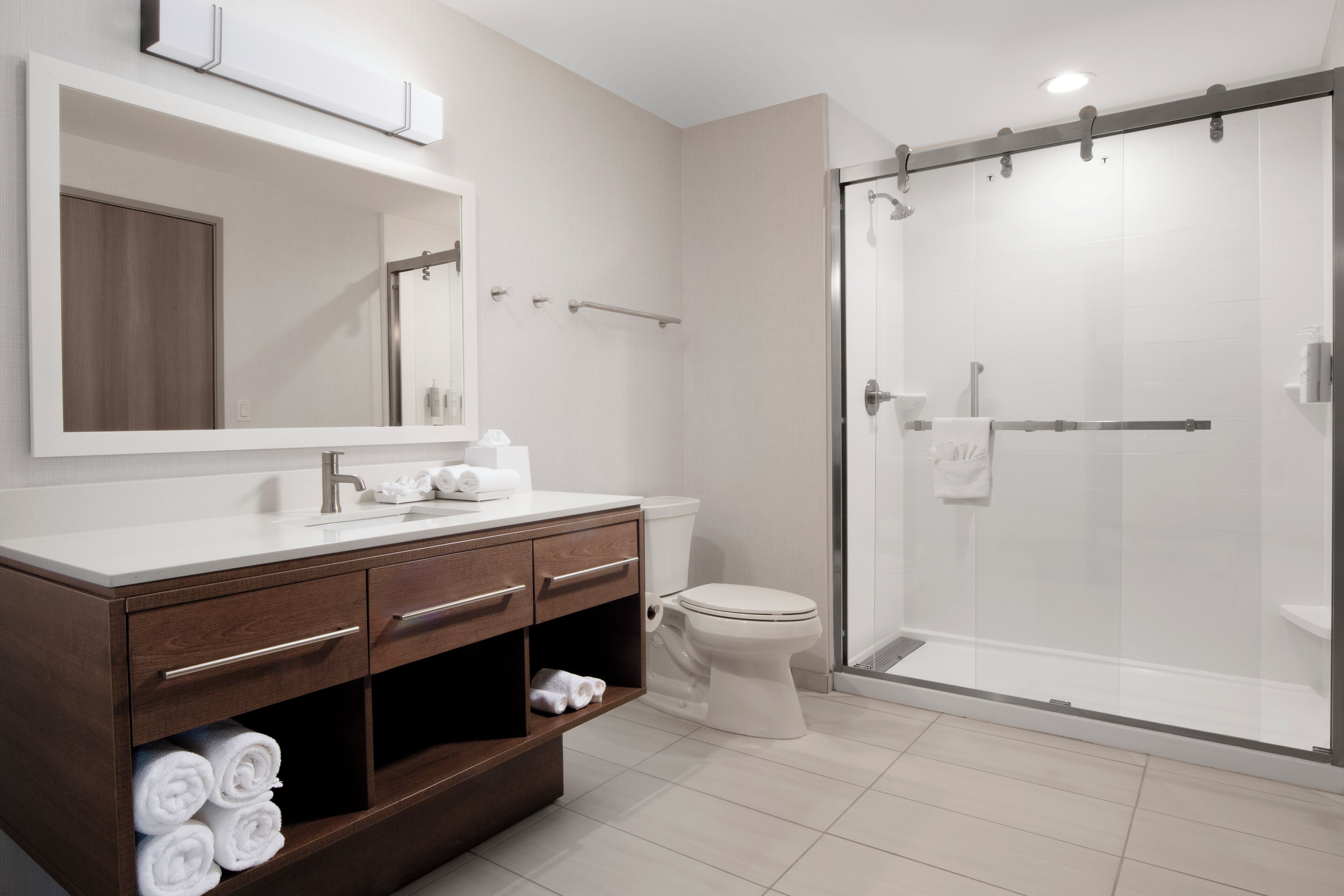 A modern bathroom with a wooden vanity, a large mirror, a toilet, and a glass-enclosed shower.