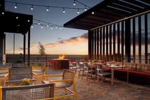 An outdoor patio area with seating, a fire pit, and a view of the sunset. - Home2 Suites By Hilton Albuquerque Airport (Albuquerque)