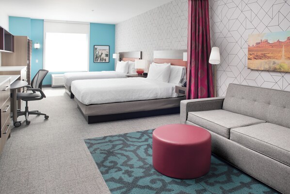 A hotel room with two beds, a desk, a chair, a sofa, and a red ottoman. - Home2 Suites By Hilton Albuquerque Airport (Albuquerque)