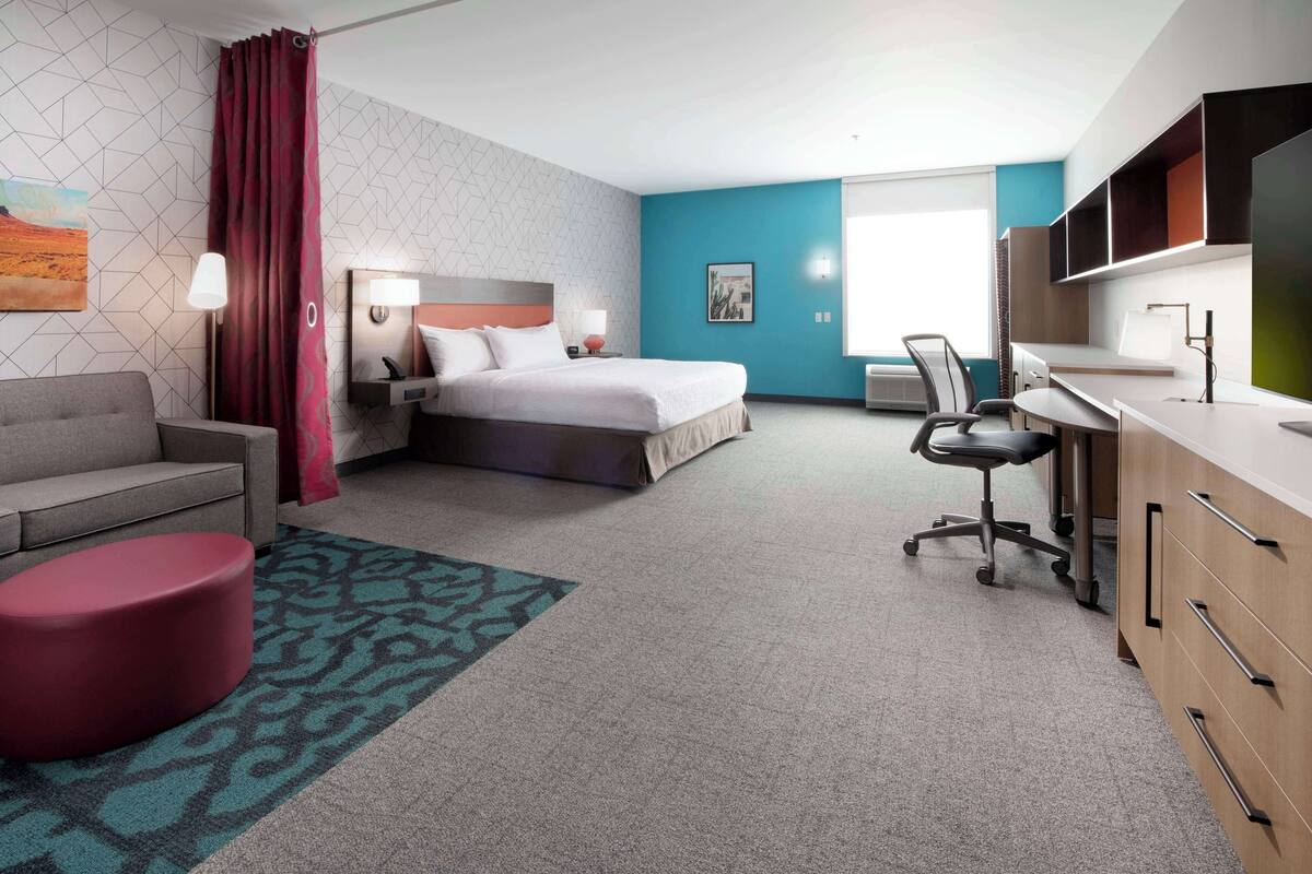 Ein Hotelzimmer mit einem Bett, einem Schreibtisch, einem Sessel, einer Couch und einem Fernseher.
