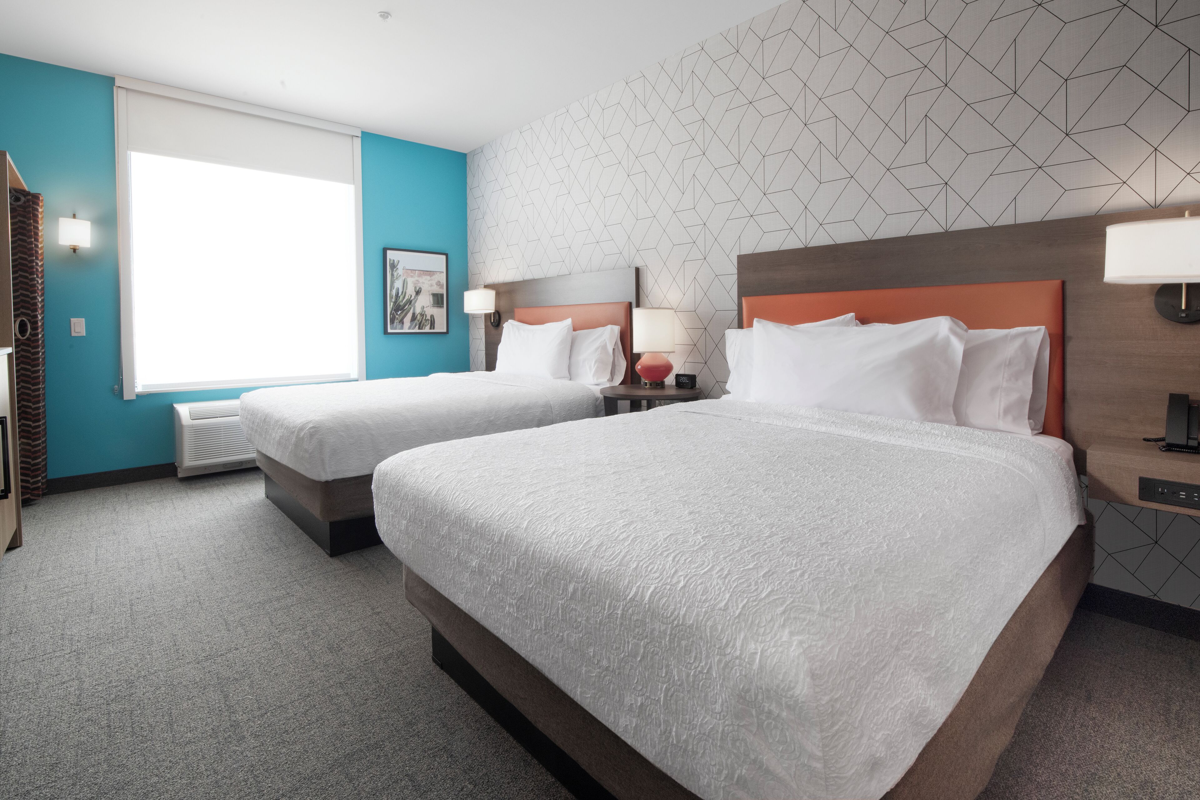 A hotel room with two beds, a large window, and a geometric wall pattern.