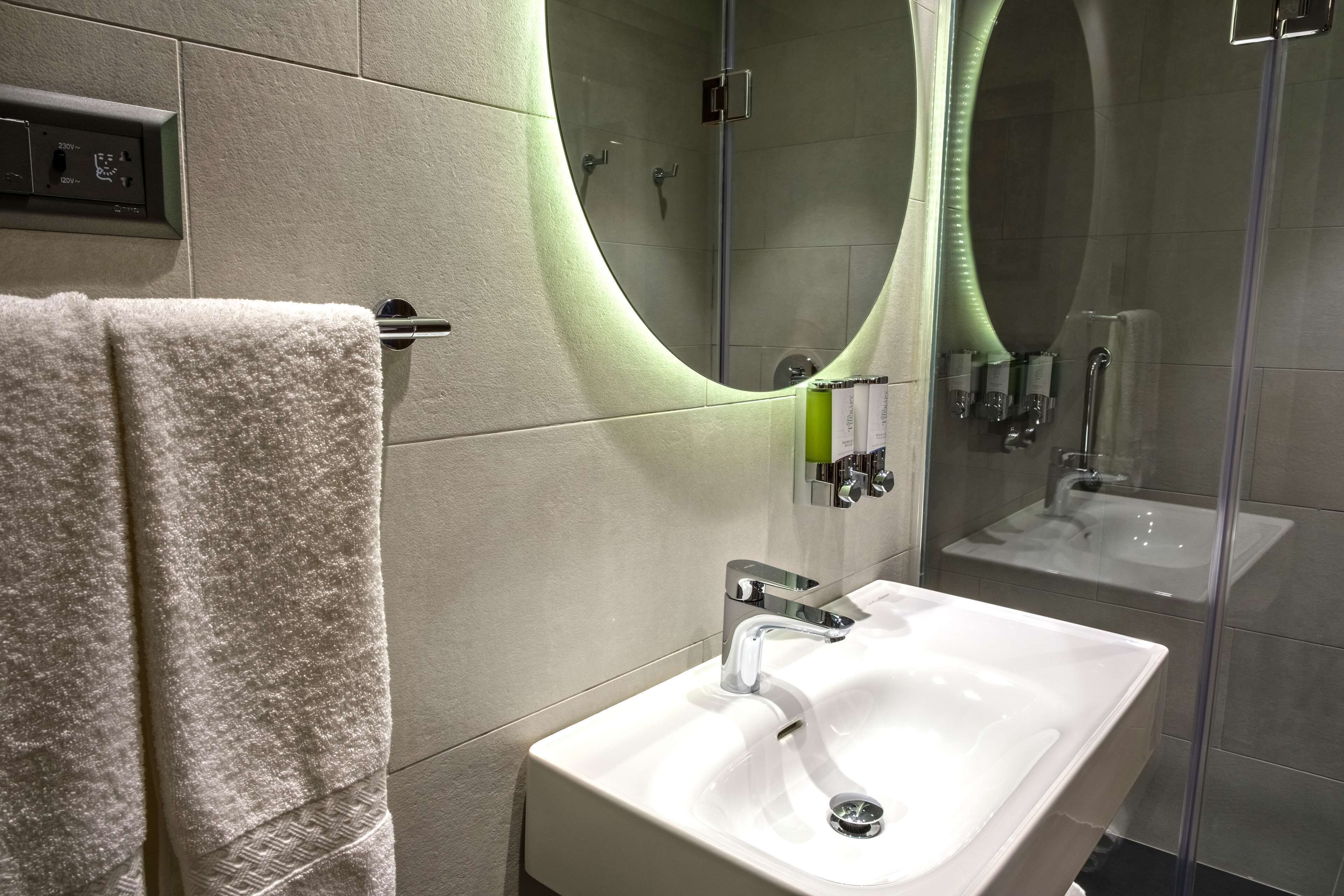 A modern bathroom with a white sink, a large mirror, and a towel rack.