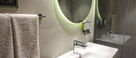 A modern bathroom with a white sink, a large mirror, and a towel rack.