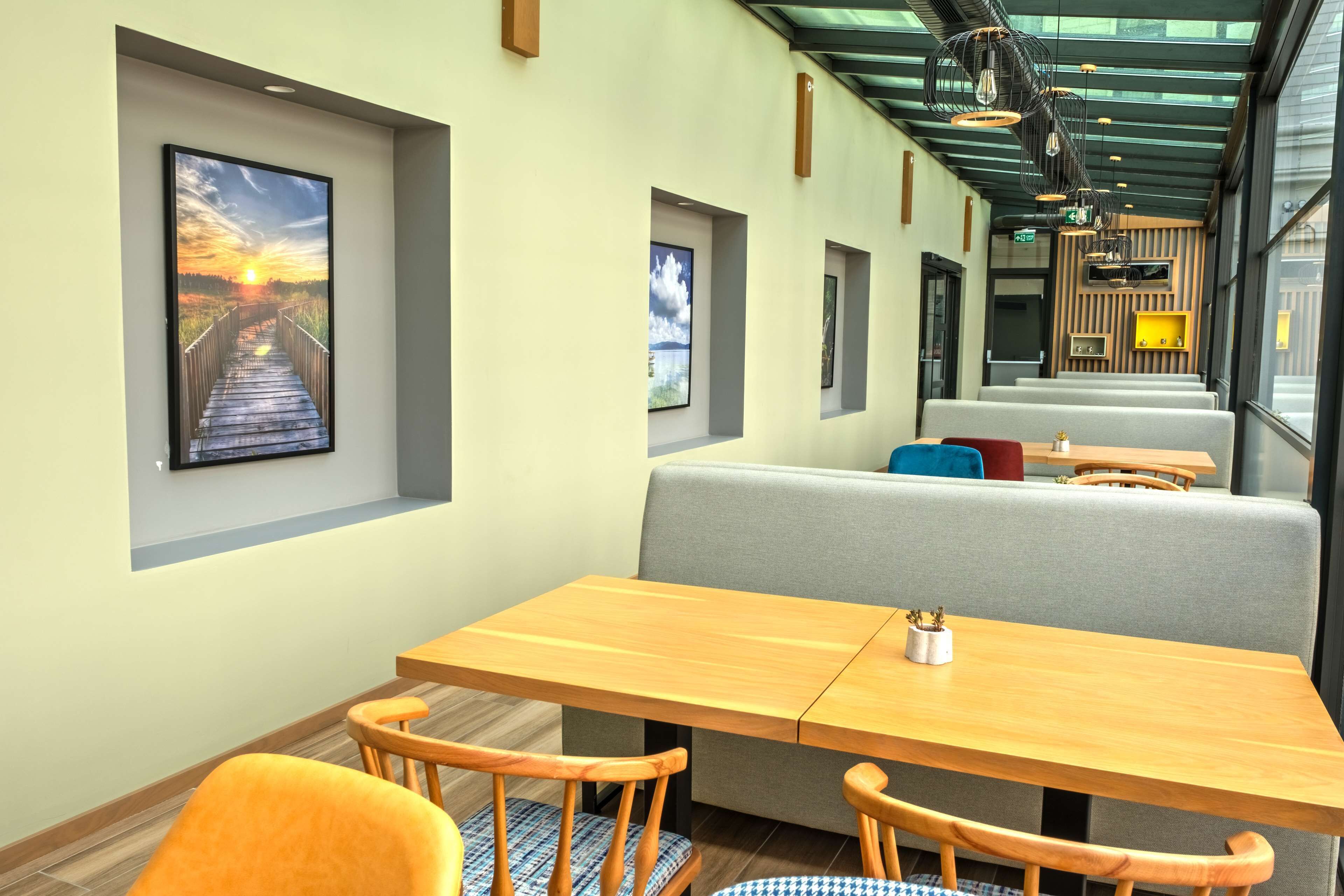 Een modern restaurant met houten tafels en stoelen, een bankje als zitgedeelte, en lijstwerk op de muren.