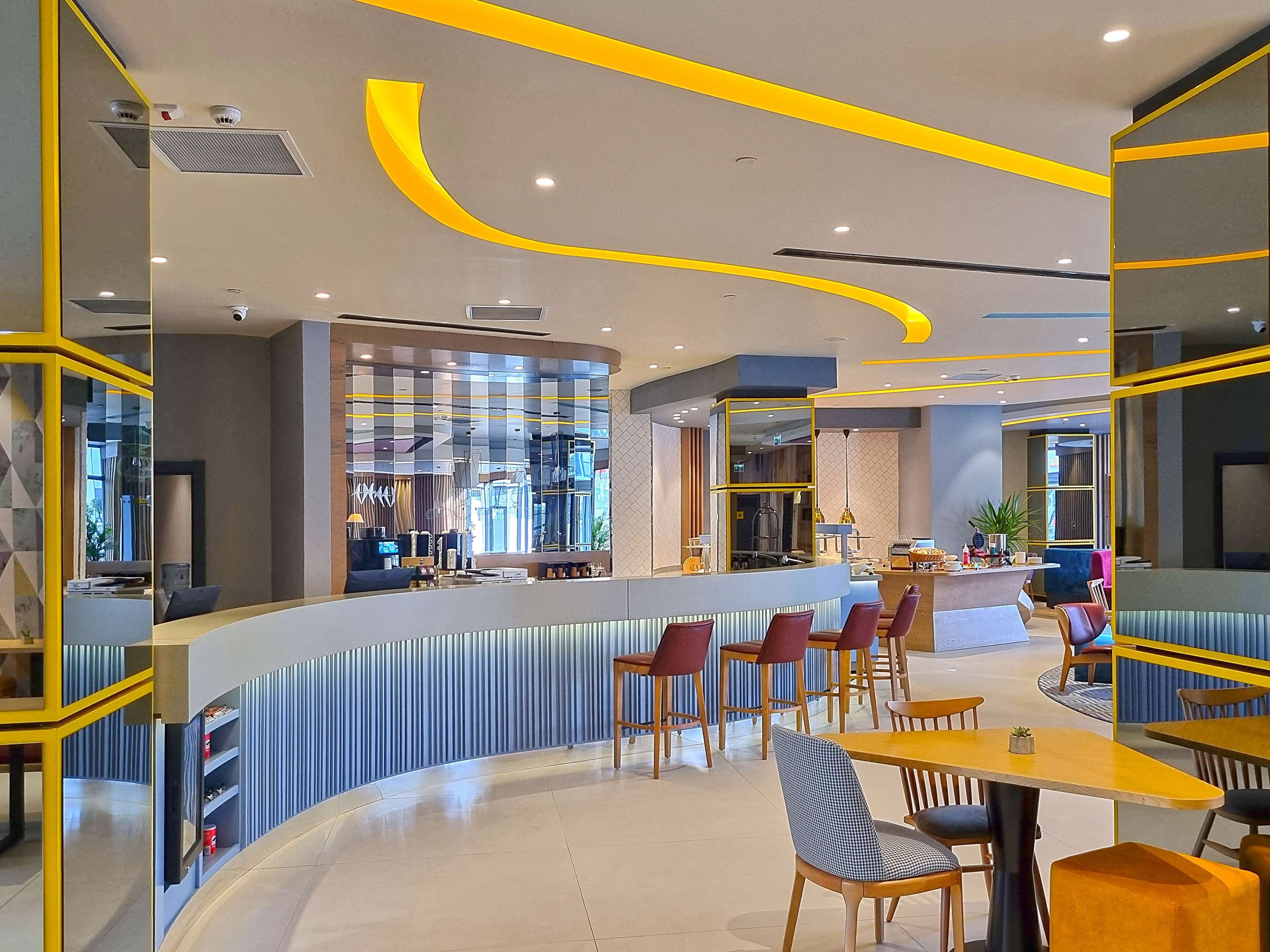 A modern restaurant with a curved counter, red and blue chairs, and yellow accents on the ceiling.