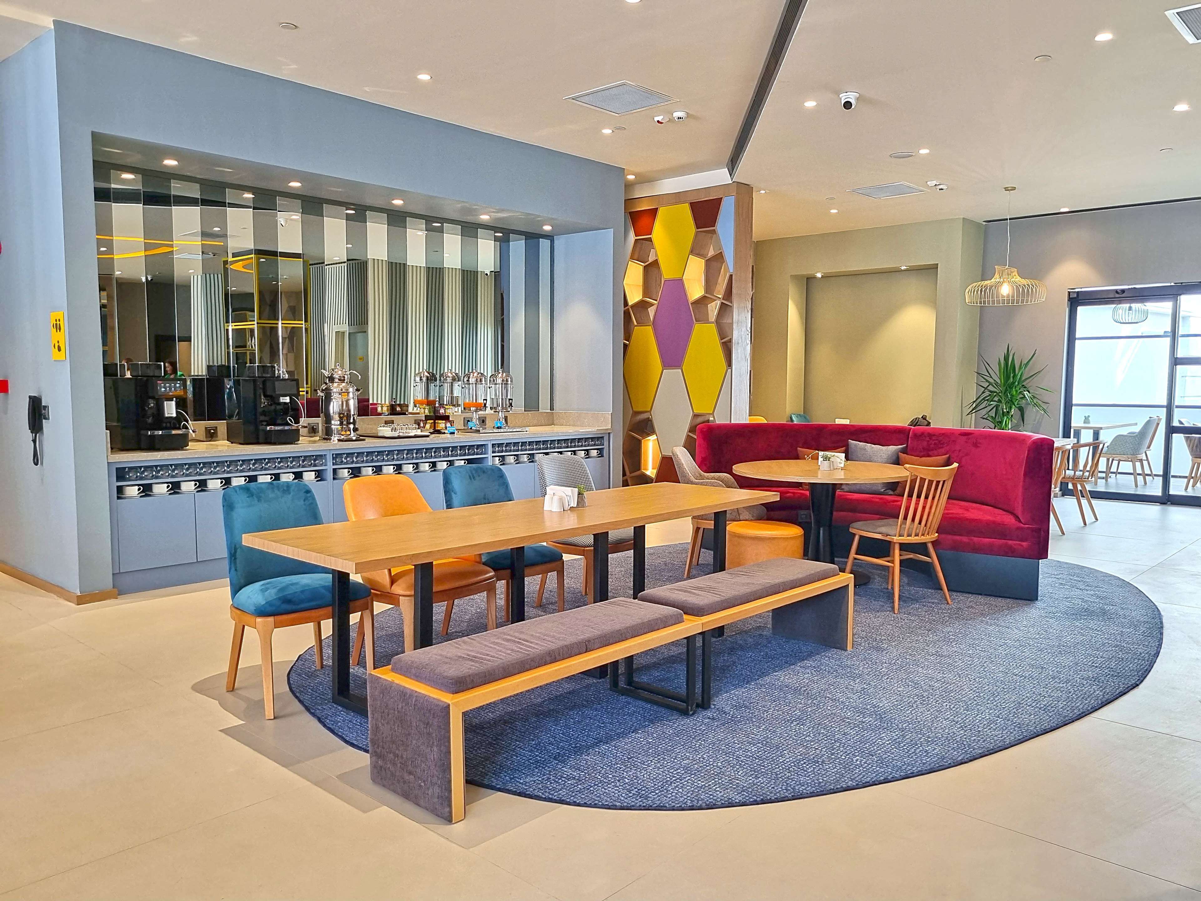 Un café moderno con zona de bar, asientos y una decoración de pared hexagonal y colorida.