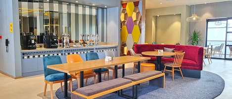 Un café moderno con zona de bar, asientos y una decoración de pared hexagonal y colorida.
