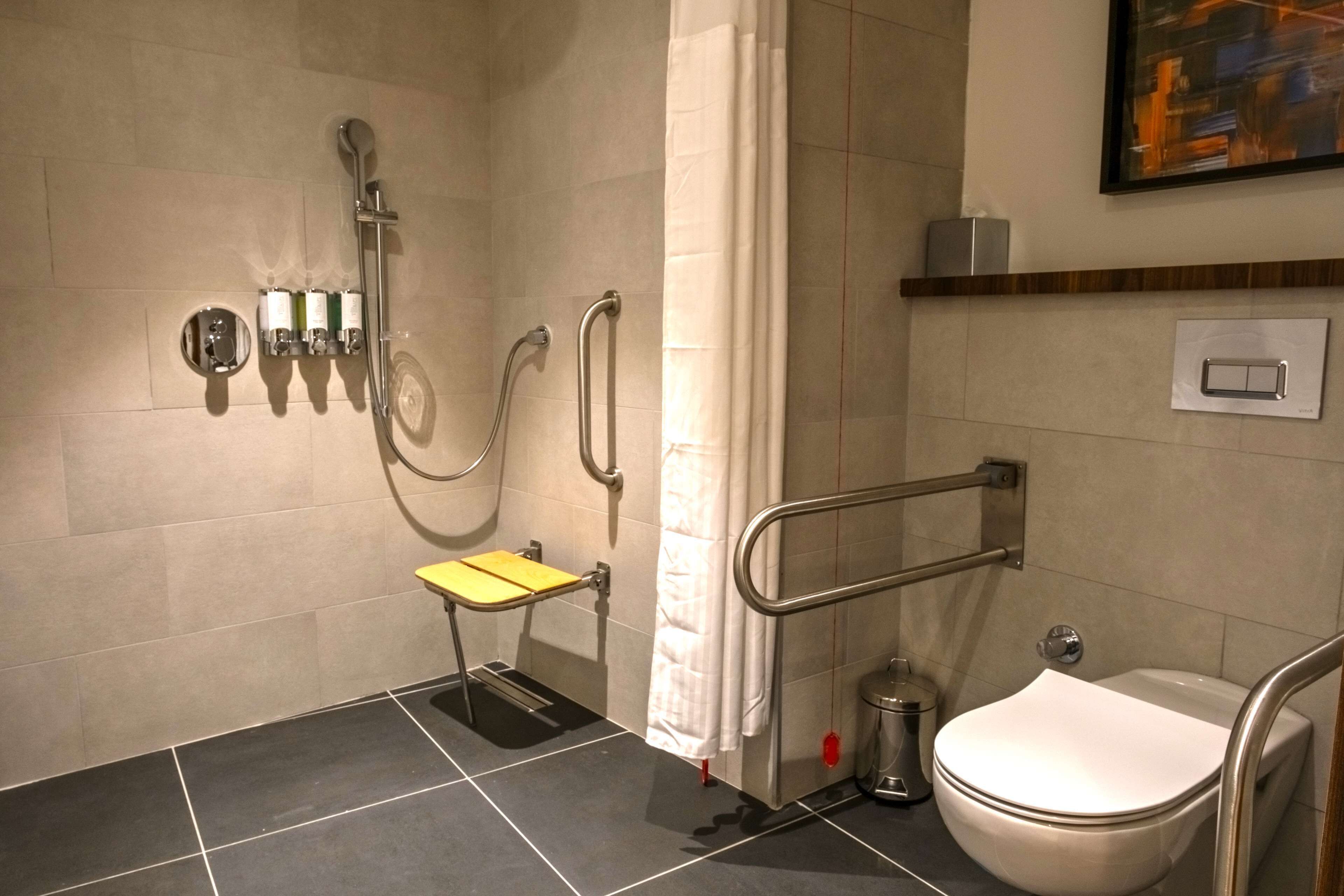 Un baño con ducha, inodoro y barras de apoyo.