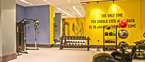 A gym with exercise equipment, including dumbbells, a rowing machine, and a wall with motivational text.