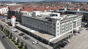 A large, white building with a prominent 'Hampton' sign, featuring a central courtyard with a fountain, surrounded by a parking lot and adjacent streets. - Hampton By Hilton Sakarya (Serdivan)