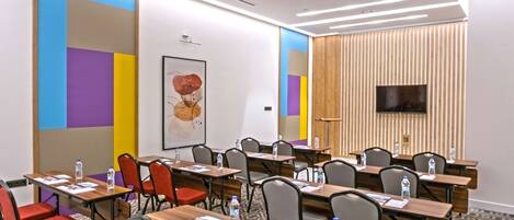 A conference room with multiple tables and chairs, a large screen, and a poster on the wall.