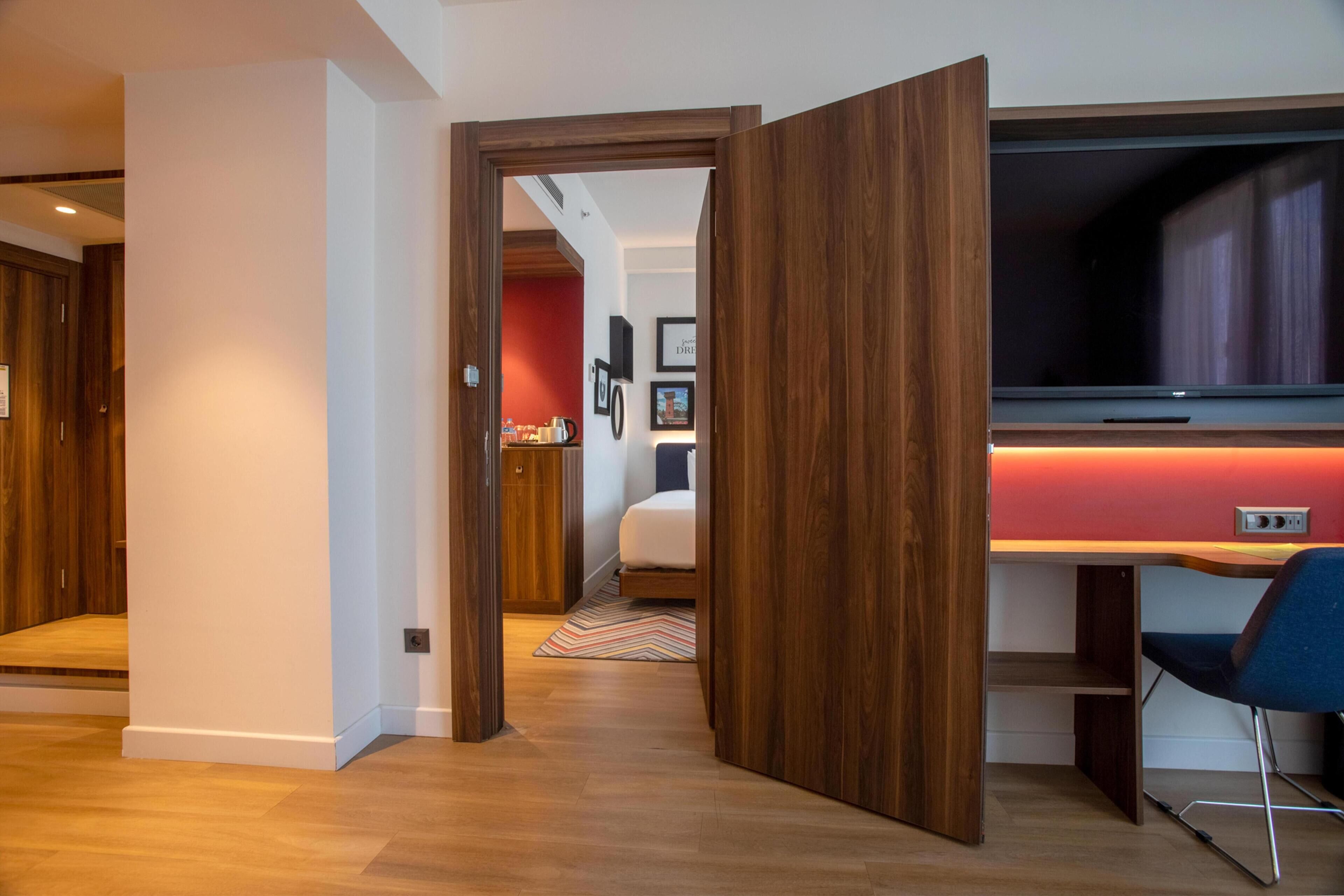 Una habitación moderna con un escritorio de madera, un televisor y una cama con un cabecero rojo.