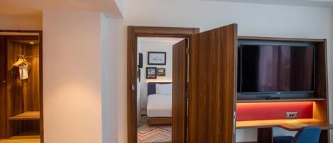 A hotel room with a wooden desk, a television, a bed, and a wardrobe.