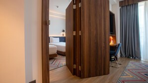 A hotel room with a wooden partition, a bed, a desk with a chair, a lamp, and a view of the outdoors. - Hampton By Hilton Sakarya (Serdivan)