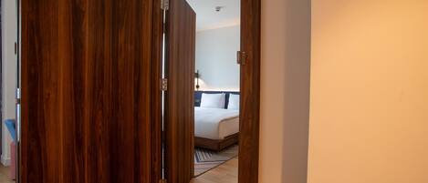 A hotel room with a wooden door, a bed with white bedding, and a striped rug on the floor.