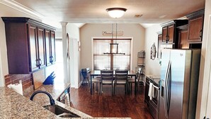 Una cocina con encimeras de granito, armarios de madera, un refrigerador de acero inoxidable y un comedor con mesa y sillas.