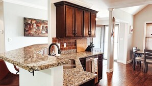 Cocina con encimeras de granito, gabinetes de madera oscura y un salpicadero de ladrillo.