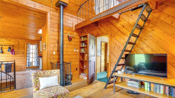 L’intérieur d’un chalet confortable, avec un canapé, un téléviseur posé sur un meuble en bois, une échelle menant à l’étage supérieur et une cheminée.