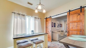 Un comedor con mesa y sillas de madera, una puerta corredera estilo granero y un ventanal con cortinas.