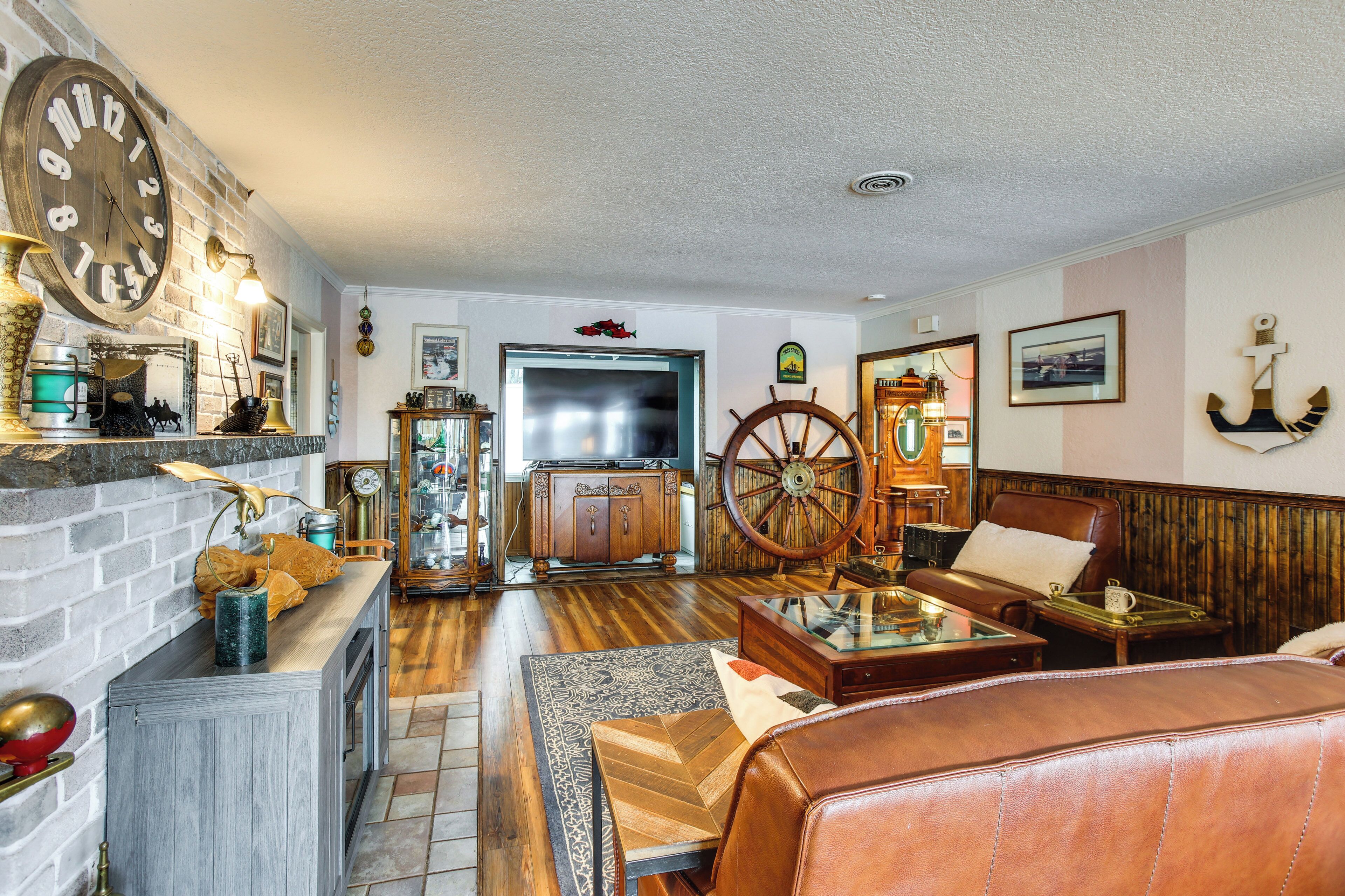 A cozy living room with a fireplace, wooden furniture, a large clock, and a ship's wheel.