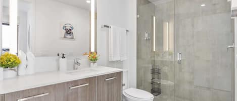Un baño moderno con cabina de ducha de vidrio, inodoro blanco y tocador con espejo y toallero.