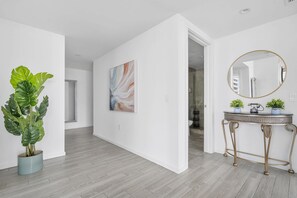 Ein modernes Interieur mit Holzboden, einem großen abstrakten Gemälde, einem runden Spiegel und einem Blumentopf.