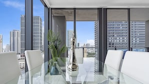 Ein modernes Interieur mit einem Glastisch, weißen Ledersesseln und Blick auf eine Stadtlandschaft durch große Fenster.