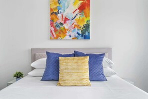 A bed with a white mattress, a grey headboard, and multiple pillows in blue and yellow.
