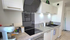 A modern kitchen with white cabinets, a black induction cooktop, a built-in oven, and a coffee machine.