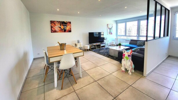 A modern living room with a dining area, a sofa, a TV, and large windows.