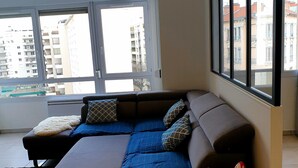 A modern living room with a sectional sofa, large windows, and a view of buildings.