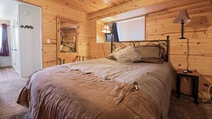 Un dormitorio de cabaña de madera con cama, mesita de noche, lámpara y ventana con cortinas.