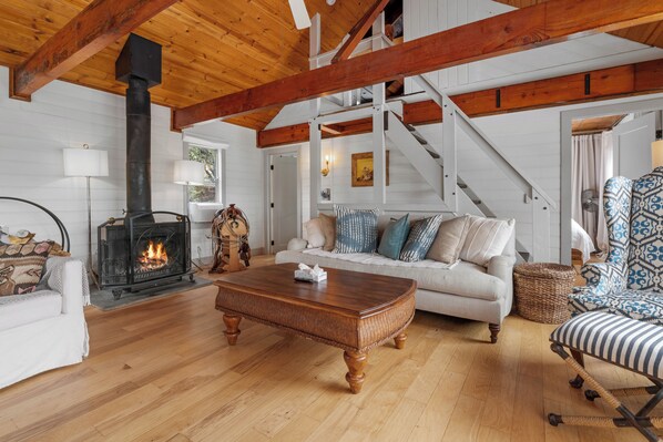 A cozy living room with a fireplace, wooden beams, a sofa, and a patterned armchair. - Enchanted Hideaway (Fawnskin)