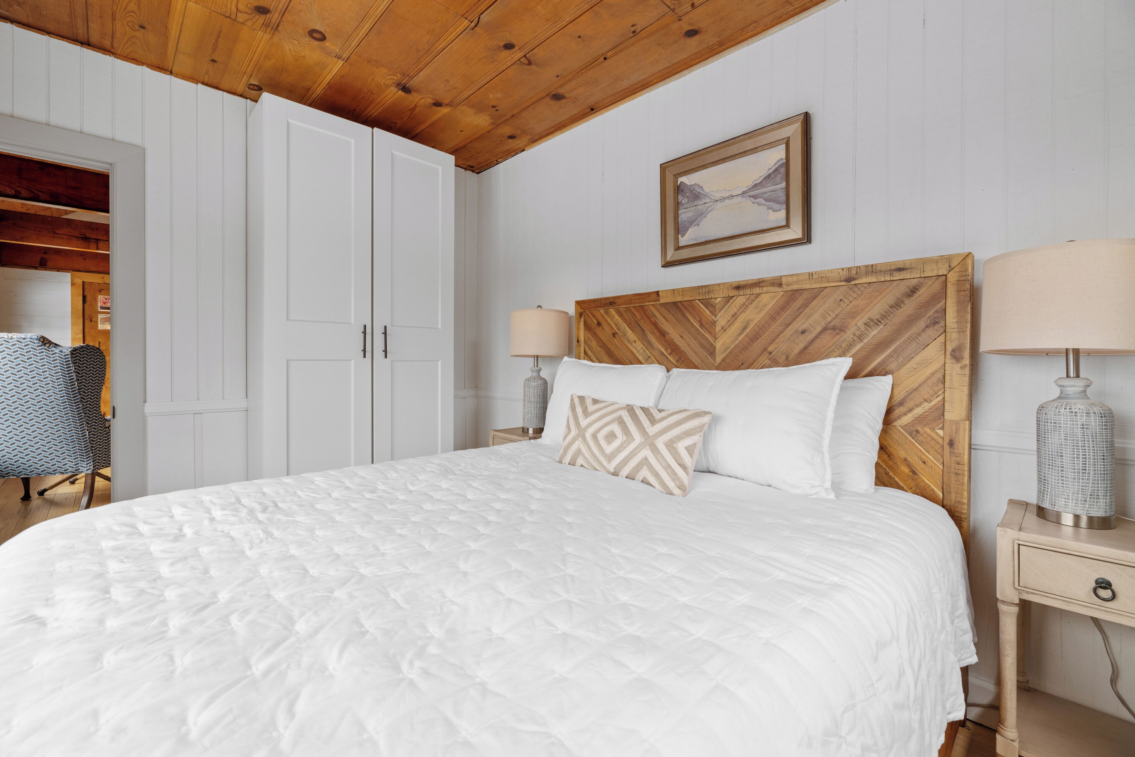 A bedroom with a wooden headboard, white bedding, and a bedside lamp.