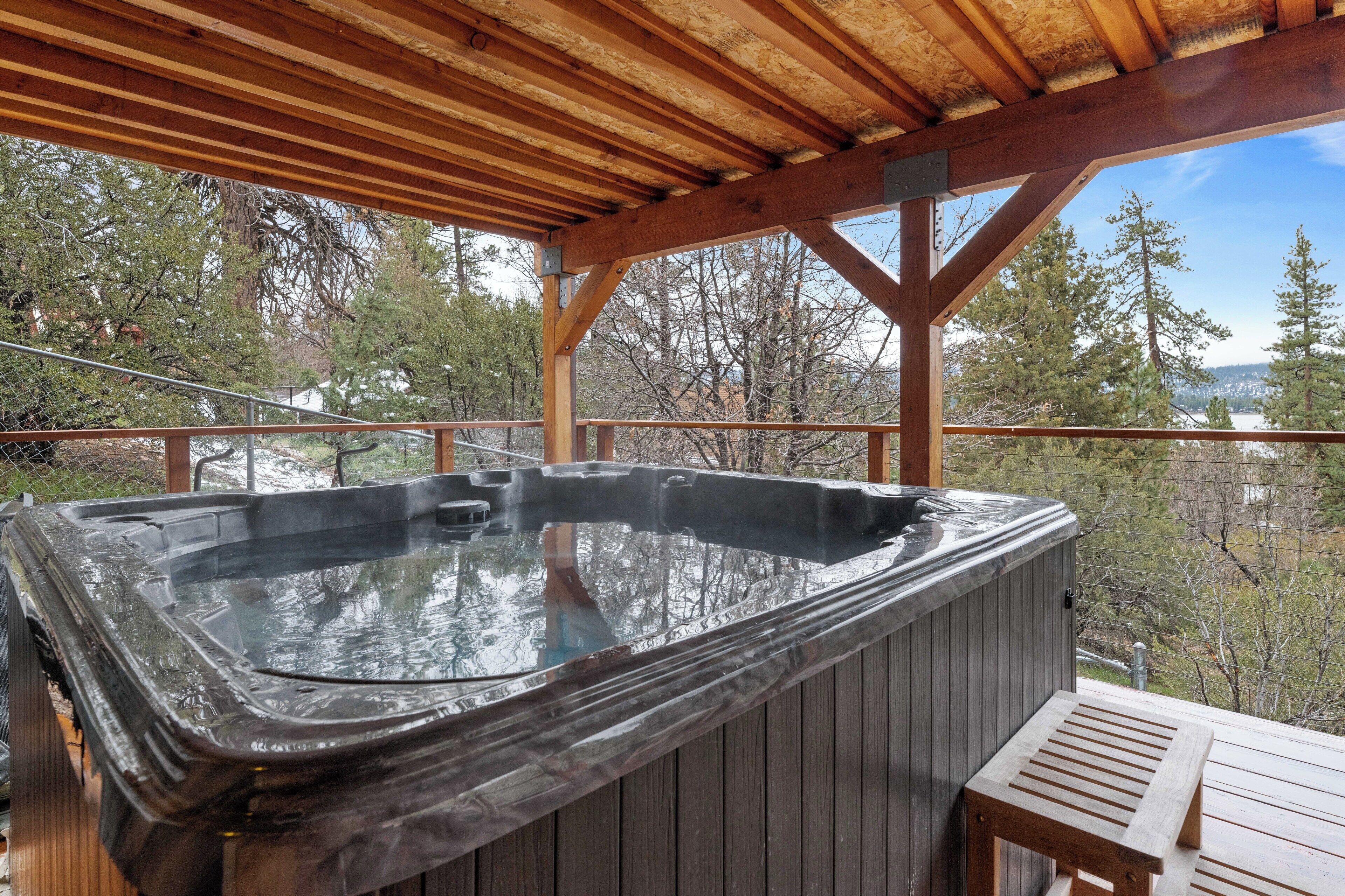 Un jacuzzi bajo una terraza de madera, con vista a árboles y un paisaje distante.