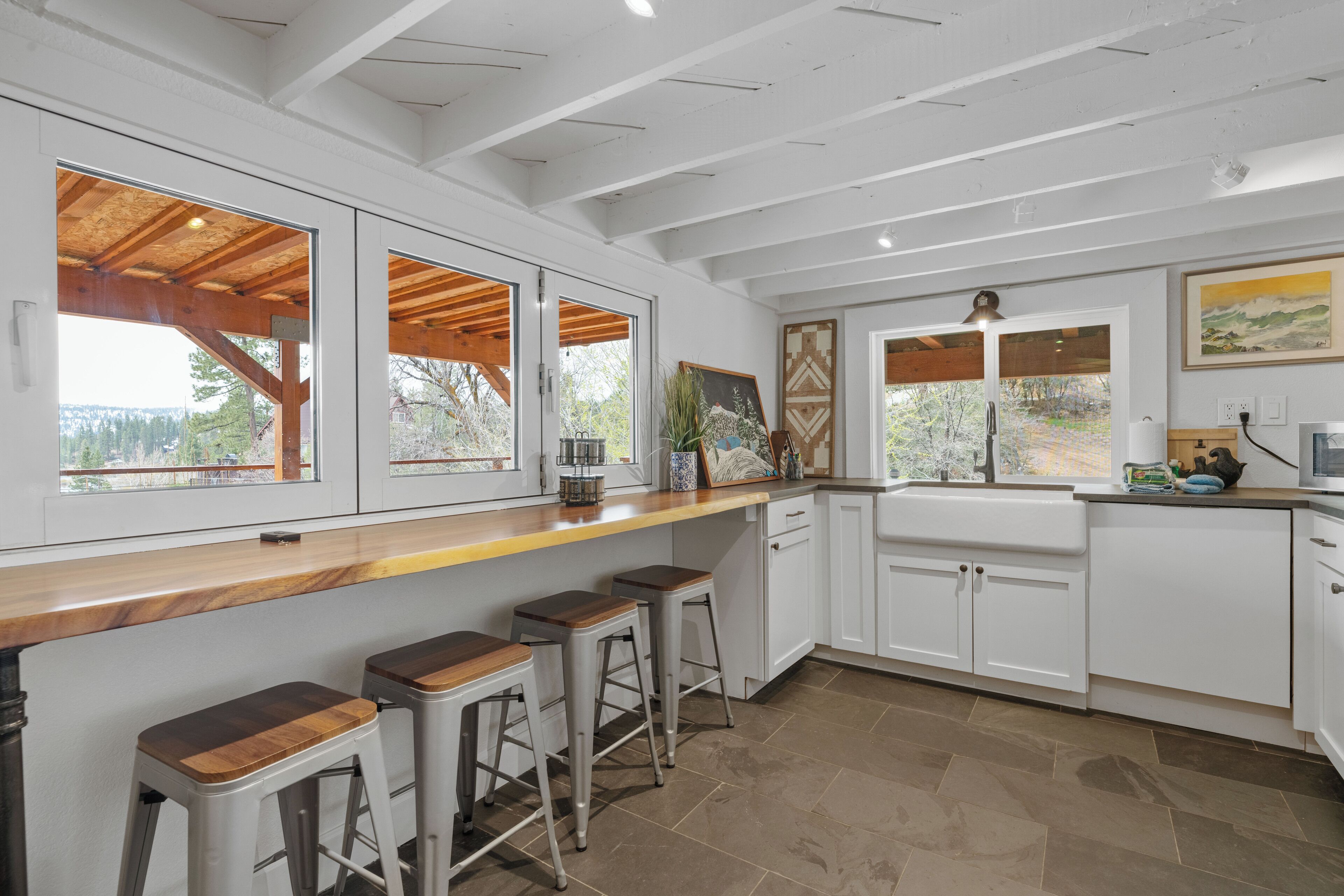Una cocina moderna con armarios blancos, una encimera de madera y un amplio ventanal con vistas a un área boscosa.