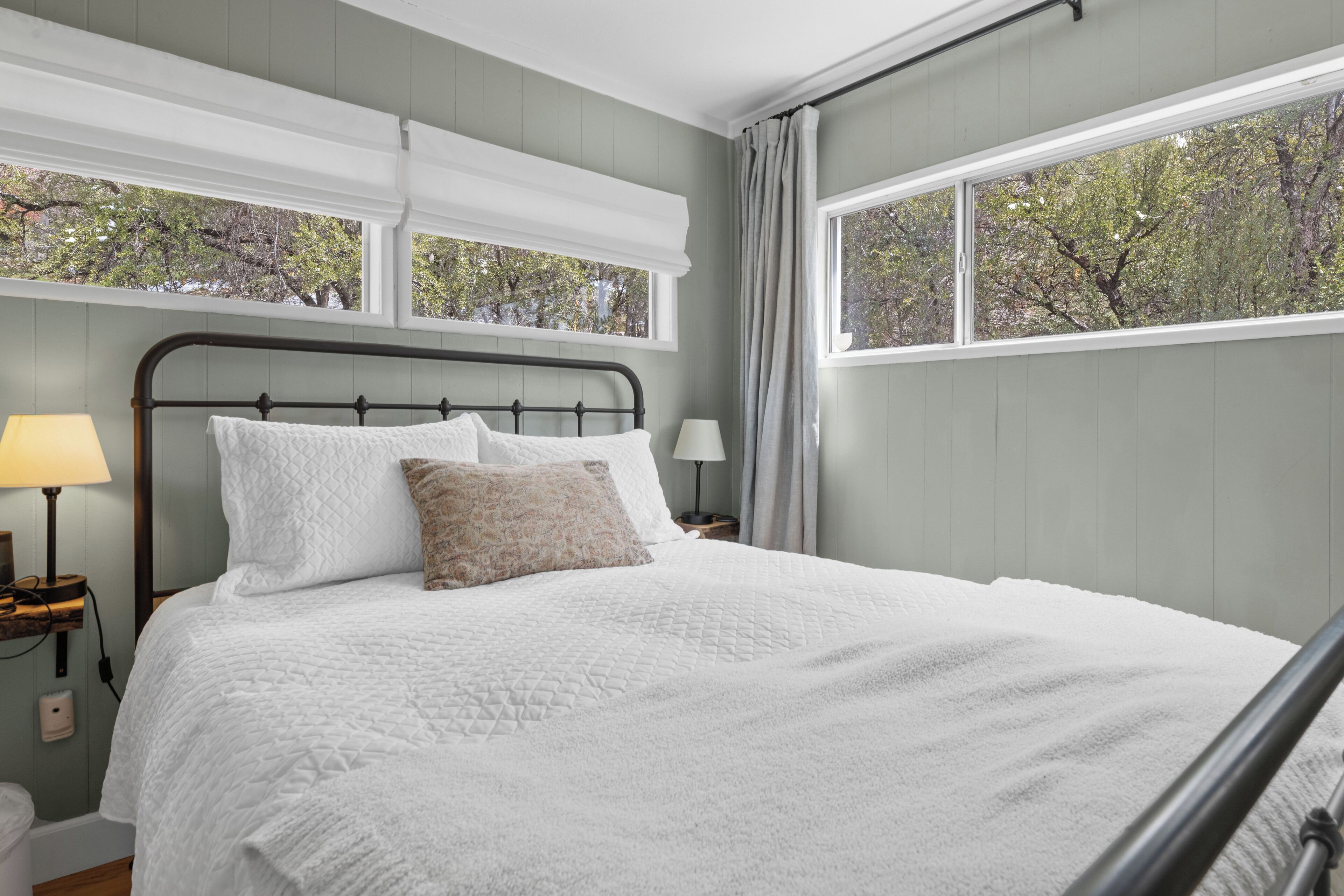 Una cama bien tendida con colcha blanca, cabecera de madera y una mesita de noche con lámpara.