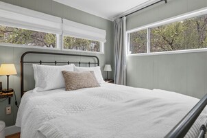 Una cama bien tendida con colcha blanca, cabecera de madera y una mesita de noche con lámpara.