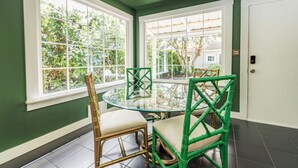 Un comedor con una mesa redonda de vidrio y sillas, ventanas grandes y una puerta.
