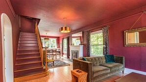 Una escalera conduce a un comedor, un sofá y una chimenea en una habitación con piso de madera y paredes rojas.