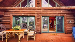 A log cabin with a wooden deck, a dining area with chairs and a table, and a sliding glass door leading to an interior space.