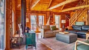 A cozy log cabin interior with a fireplace, leather sofas, and a wooden staircase.