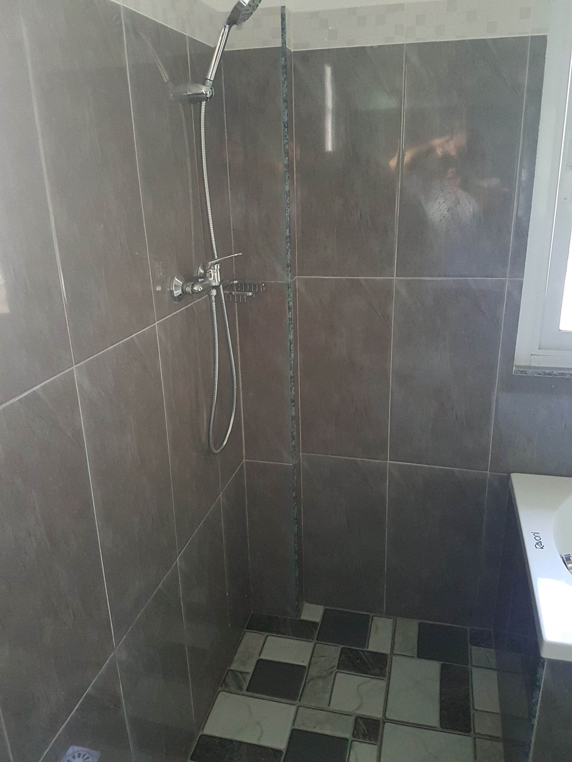 Een klein betegeld douchegedeelte met een handdouche en een kraan op de muur.