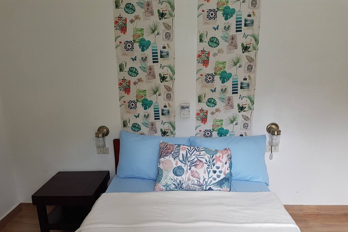 A bedroom with a bed, a nightstand, and a wall with patterned curtains.