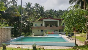 A two-story building with a swimming pool, surrounded by palm trees and greenery. - Hotel Pentaqua (Irosin)