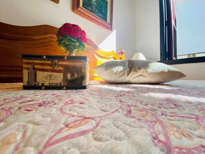 A suitcase with a New York City design, a vase with red flowers, and a decorative pillow on a bed with a patterned bedspread. - EXCELENTE OPÇAO - 03 quadras RUA COBERTA (Gramado)