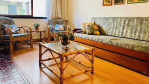 Ein Wohnzimmer mit einer Couch, zwei Sesseln, einem Couchtisch und einem Fenster mit Vorhängen.